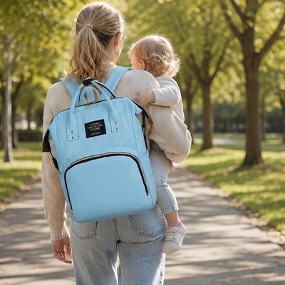 maman portant bébé et sac a dos a langer bleu au parc
