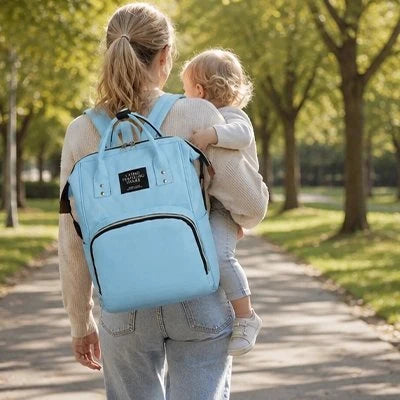 maman portant bébé et sac a dos a langer bleu au parc