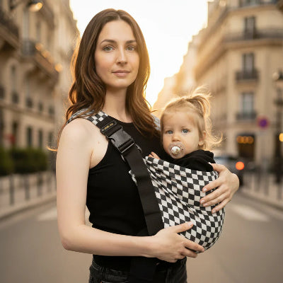une maman qui porte son bébé dans une echarpe de portage damier